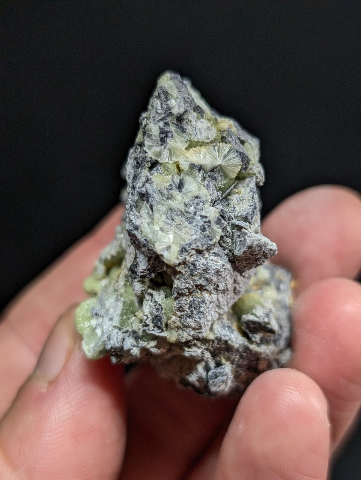 A rough, irregularly shaped mineral specimen with a grayish matrix and translucent green crystalline formations.