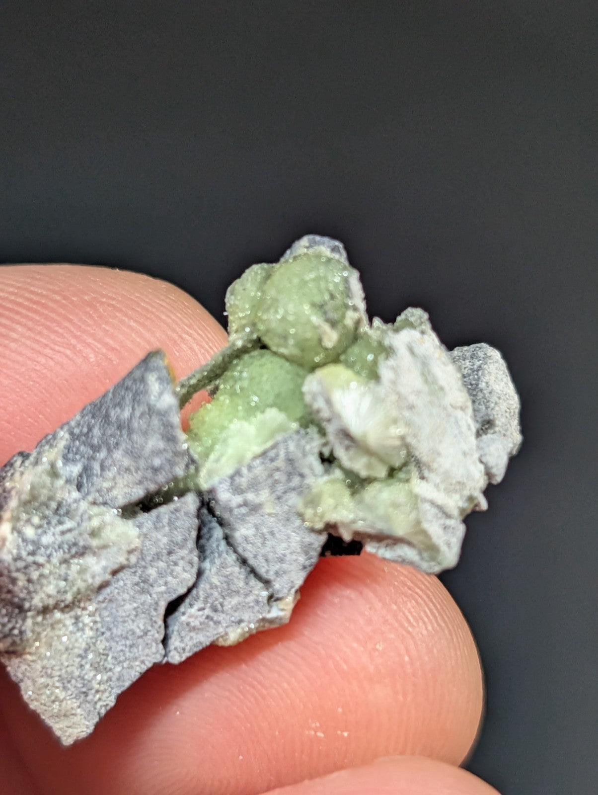 A rough, irregularly shaped mineral specimen with a grayish base and patches of pale green crystalline growths.