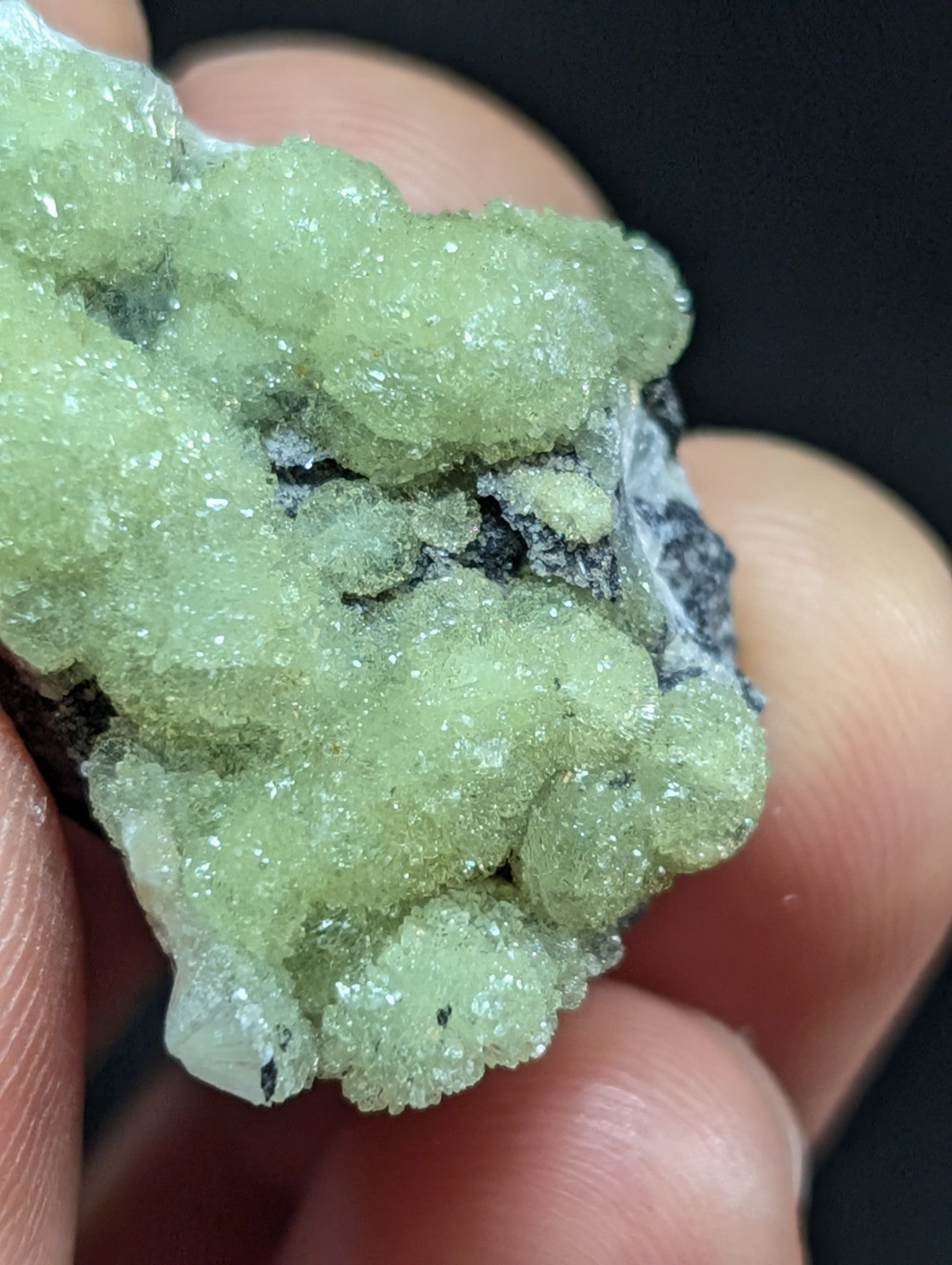 A translucent green crystalline mineral specimen with a rough, clustered texture and embedded dark matrix.