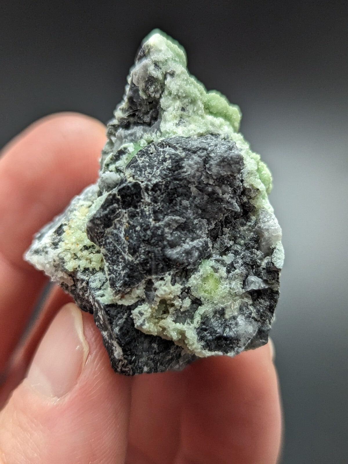 A rough, irregularly shaped mineral specimen featuring a striking contrast between dark gray to black matrix and vibrant light green crystalline formations.