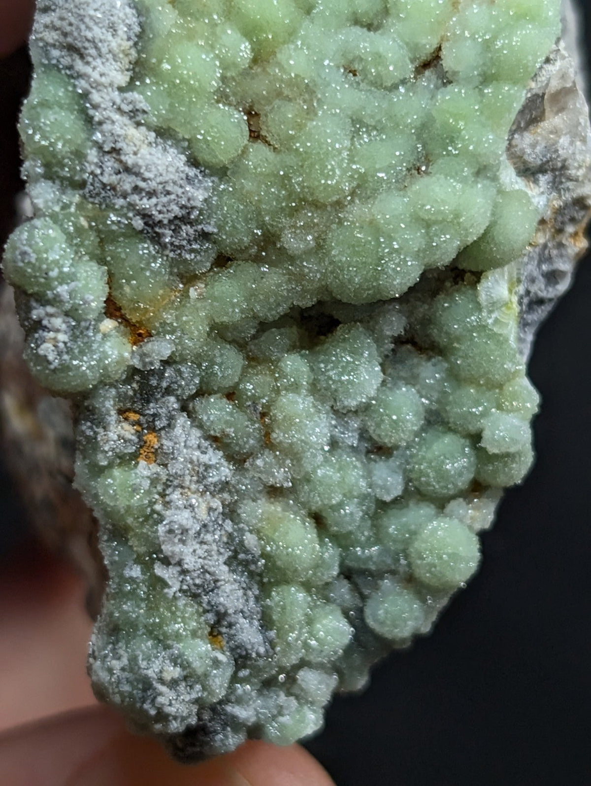 A cluster of translucent green crystals with a sparkling, granular texture and patches of grayish matrix.