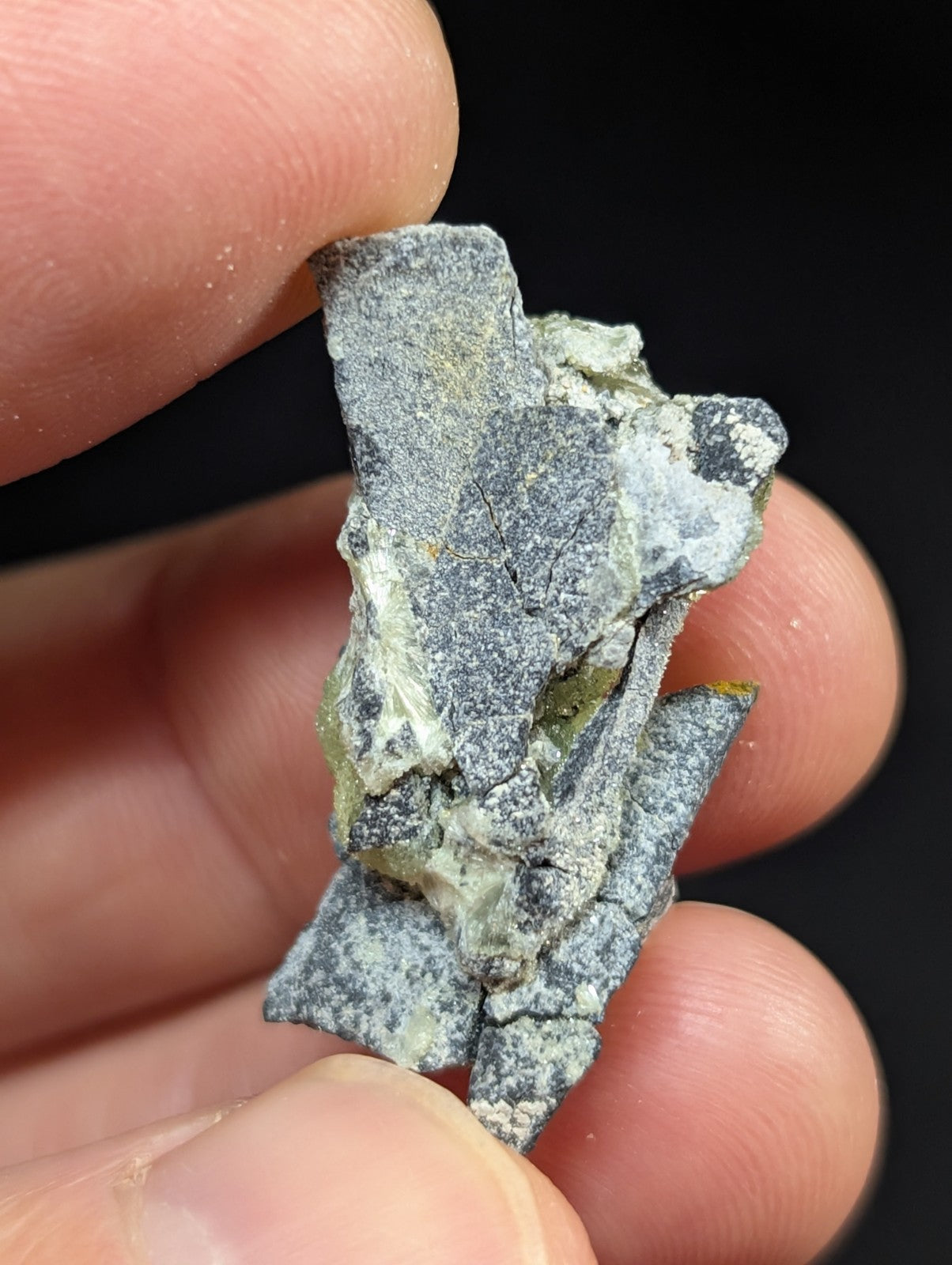 A rough, irregularly shaped gray mineral specimen with patches of white and subtle greenish hues.