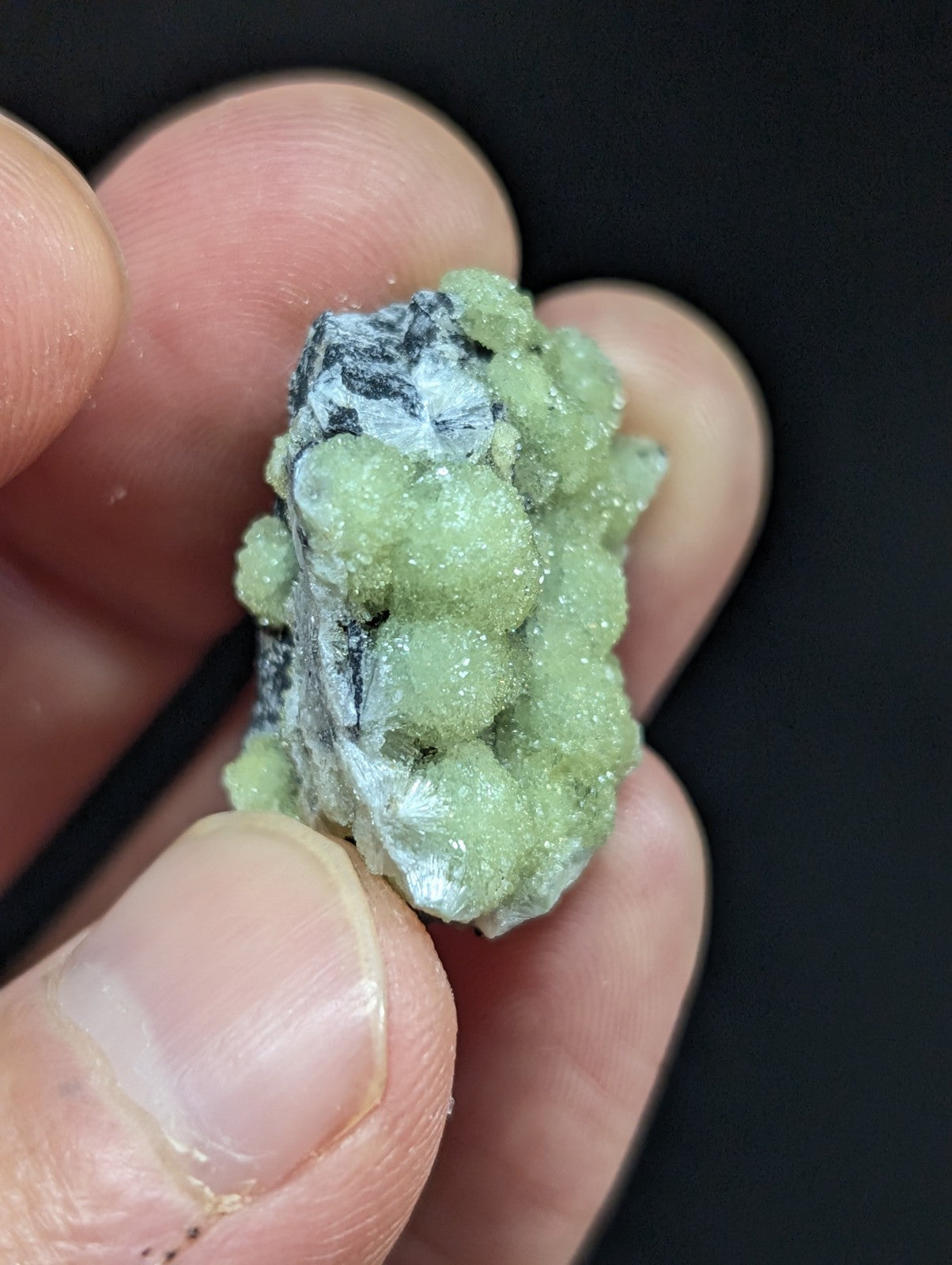 A cluster of pale green, crystalline mineral formations with a rough, textured surface and some white or grayish matrix material.