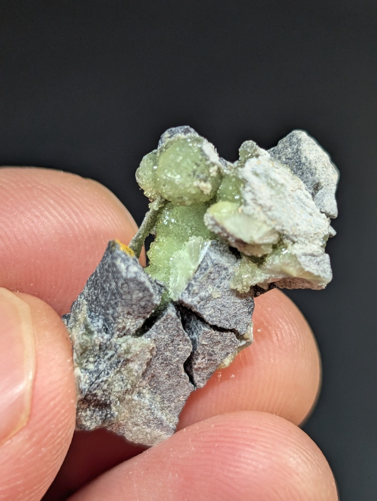 A rough, irregularly shaped mineral specimen featuring a cluster of translucent green crystals embedded in a grayish matrix.