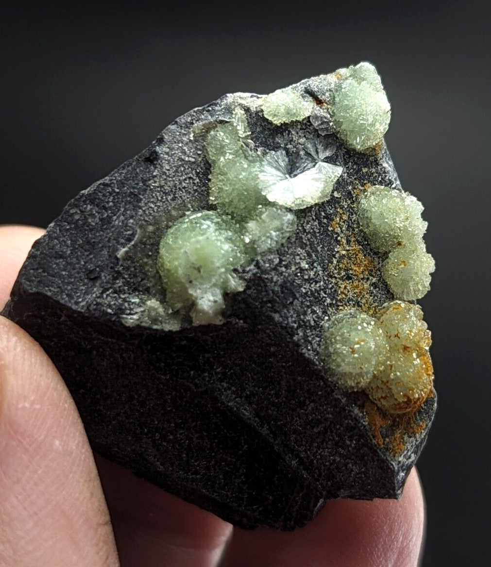 A dark, rough-textured rock specimen featuring clusters of translucent green crystals with some exhibiting a subtle yellowish tint.