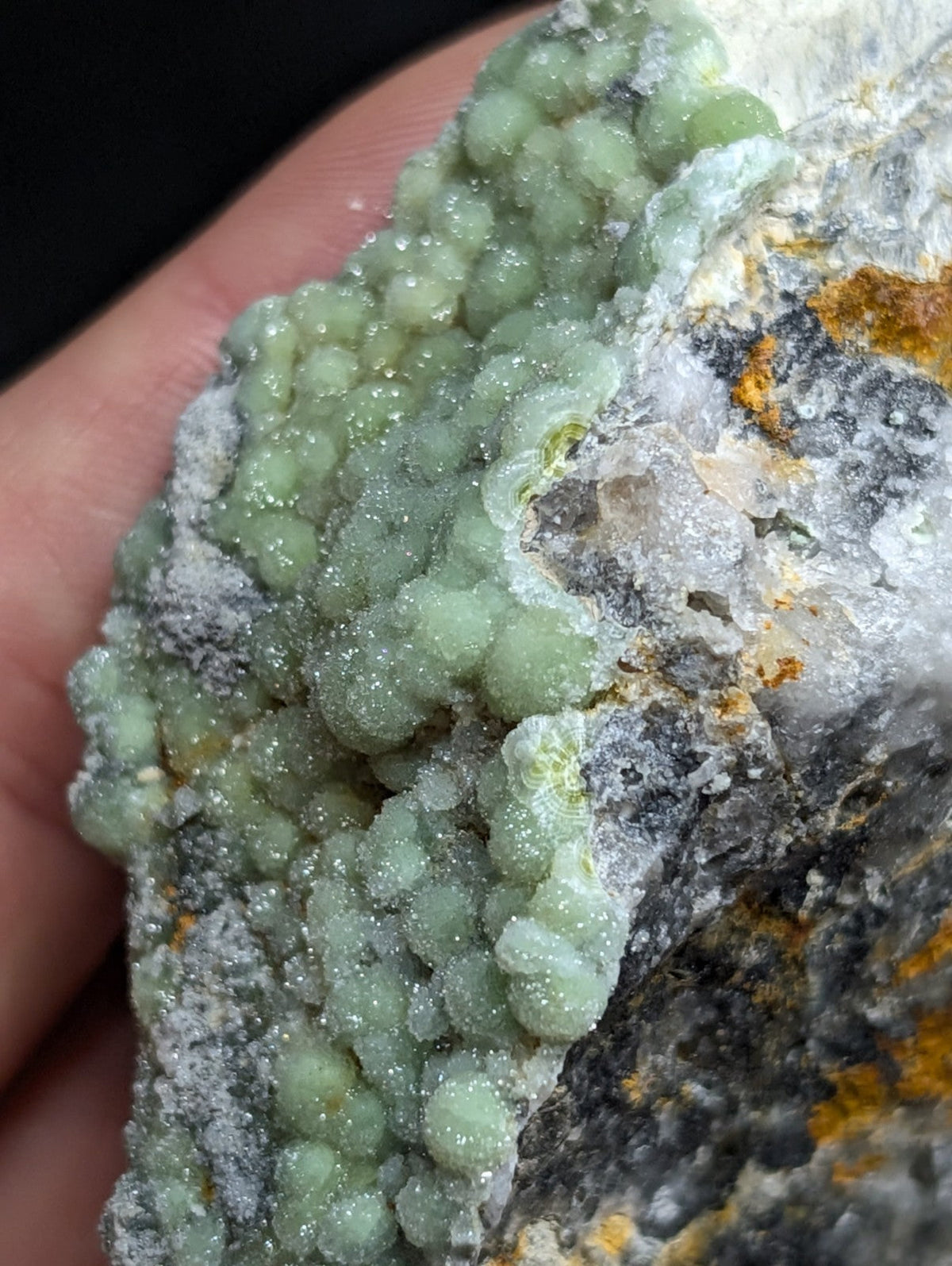 A cluster of translucent, pale green mineral crystals with a sugary texture grows densely on a rougher gray and white rock matrix.