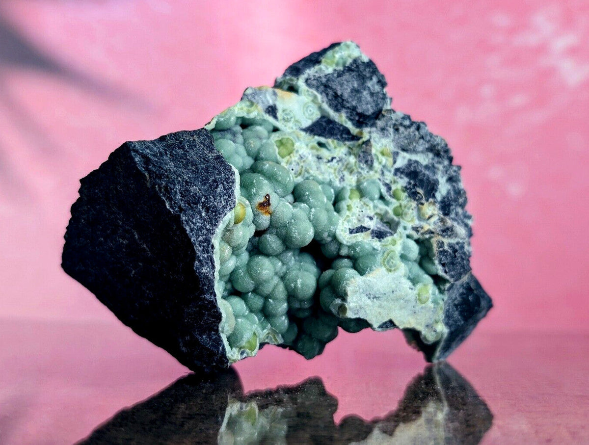 A striking green and black mineral specimen featuring a cluster of spherical, bead-like formations nestled within a dark matrix.
