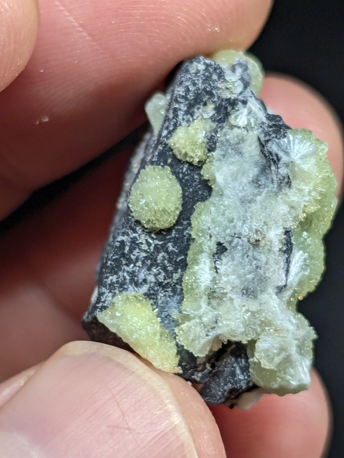A dark gray rock specimen featuring light green, crystalline formations with a rough, textured surface.