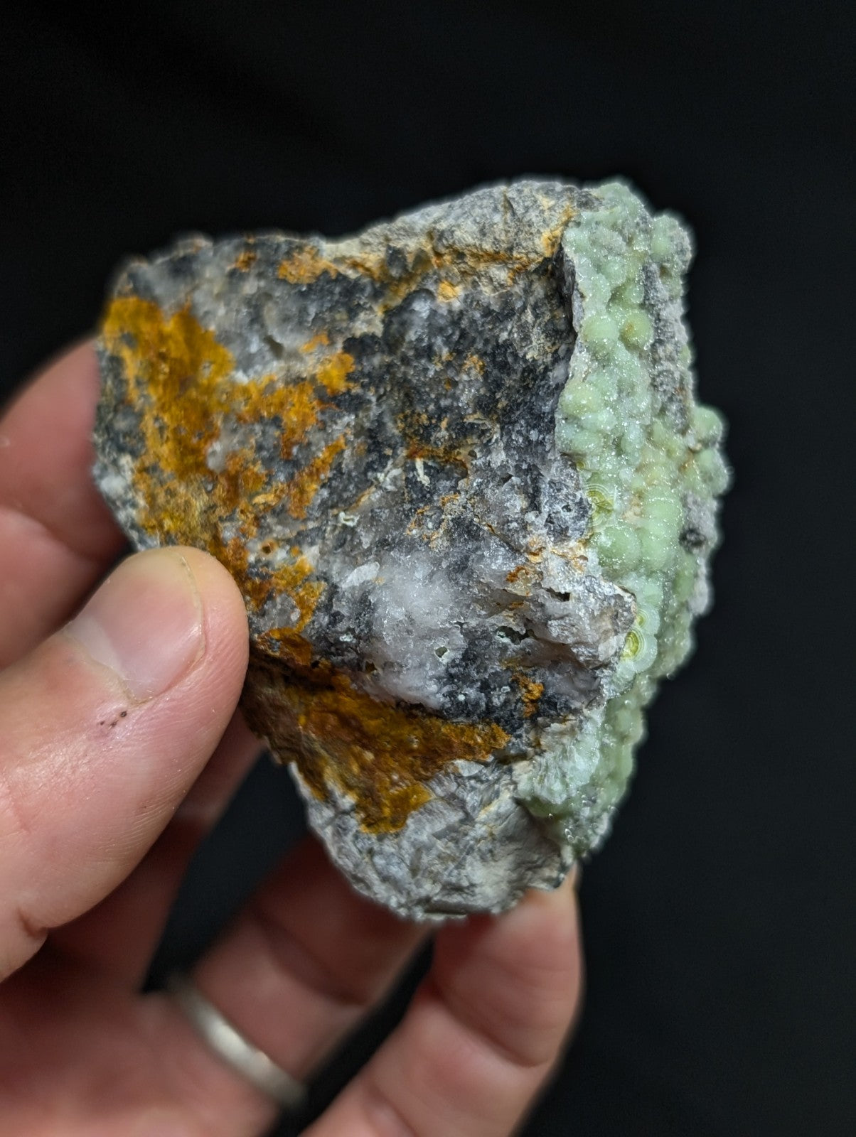 A rugged, irregularly shaped rock specimen featuring patches of vibrant orange and pale green mineral growths against a grayish base.