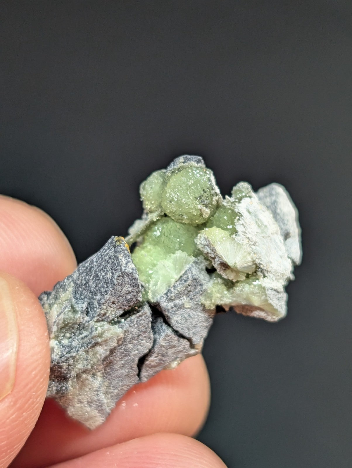 A cluster of translucent green crystals growing from a rough, gray rock matrix.