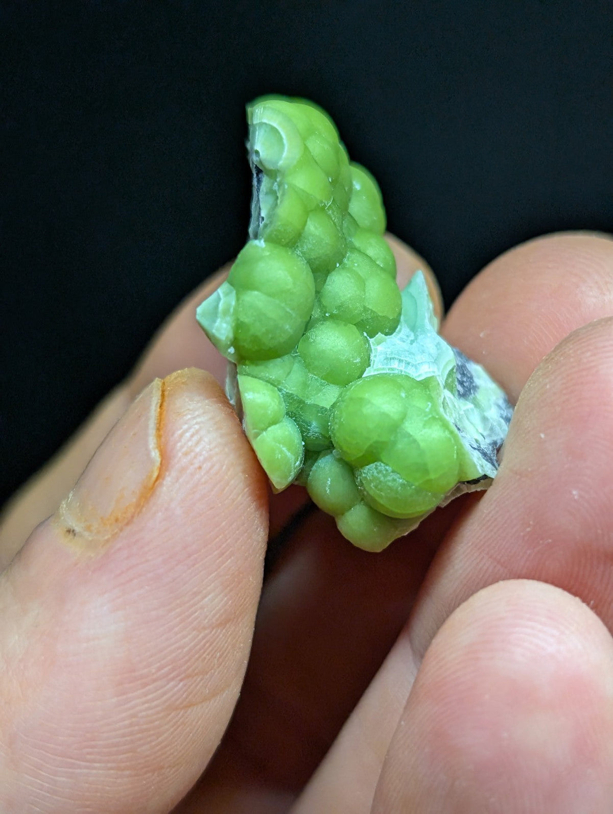 A vibrant green, bumpy mineral specimen with a glossy surface and some white crystalline patches.