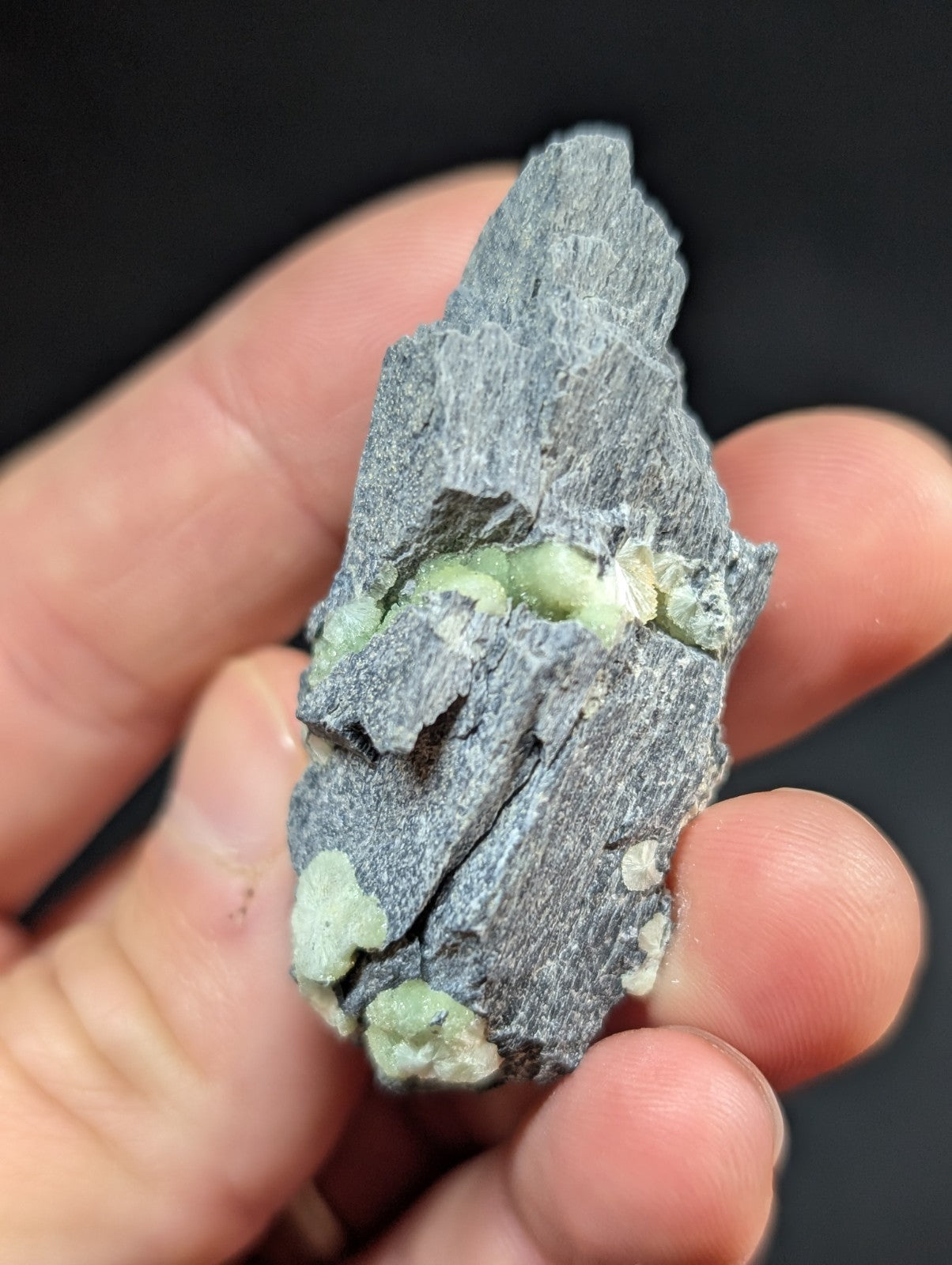 A rough, dark gray rock specimen with embedded light green mineral crystals.