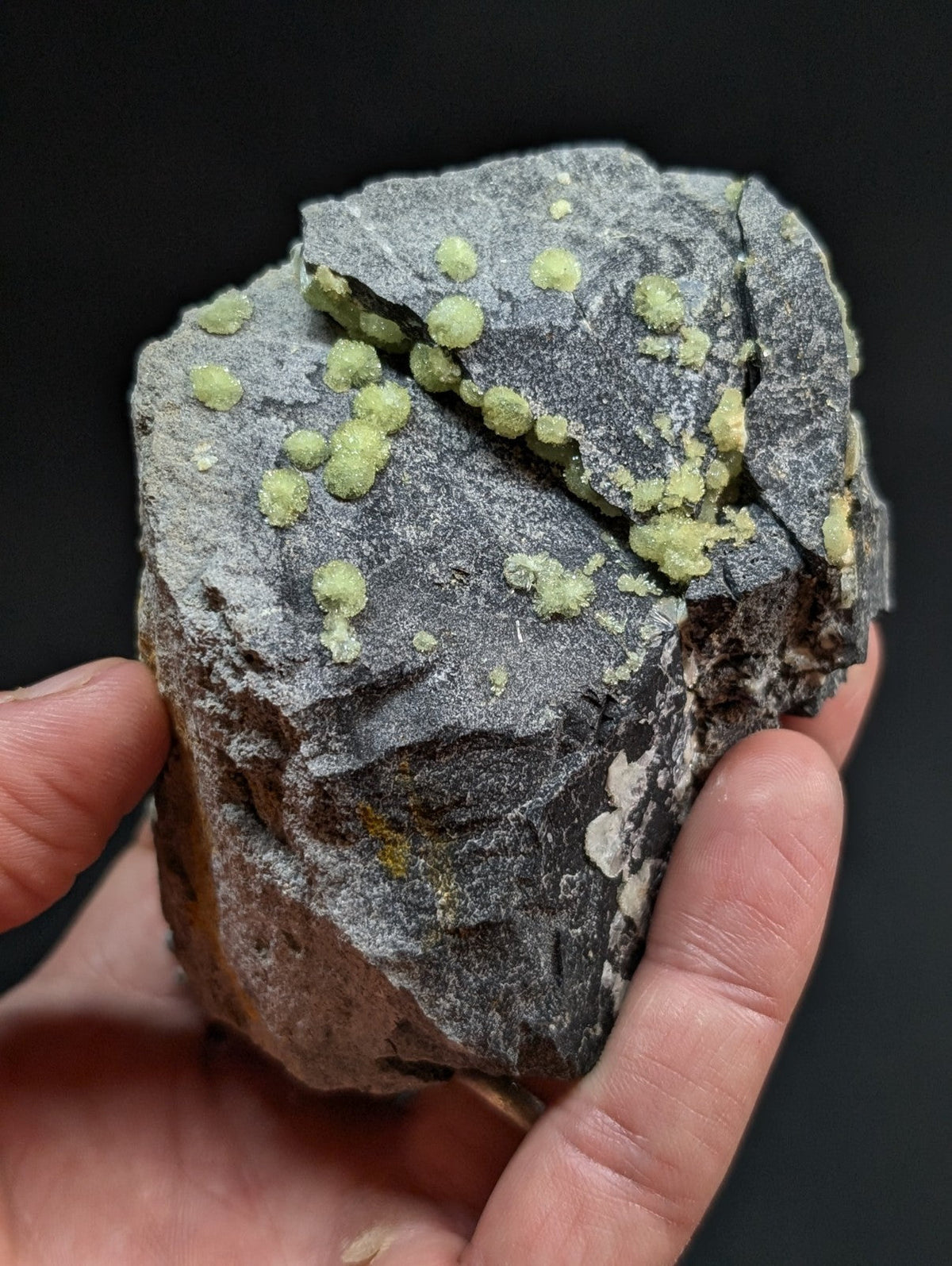 A rough, dark gray rock specimen featuring scattered bright green crystalline formations.