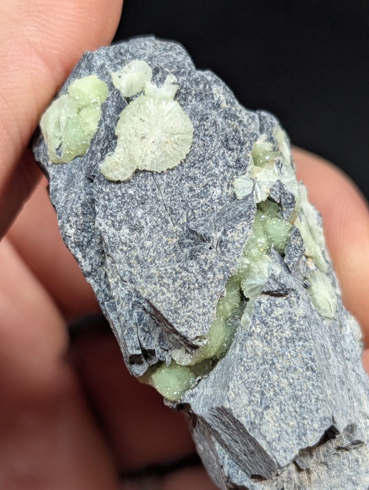 A gray rock specimen featuring light green, crystalline mineral formations with a rough, textured surface.