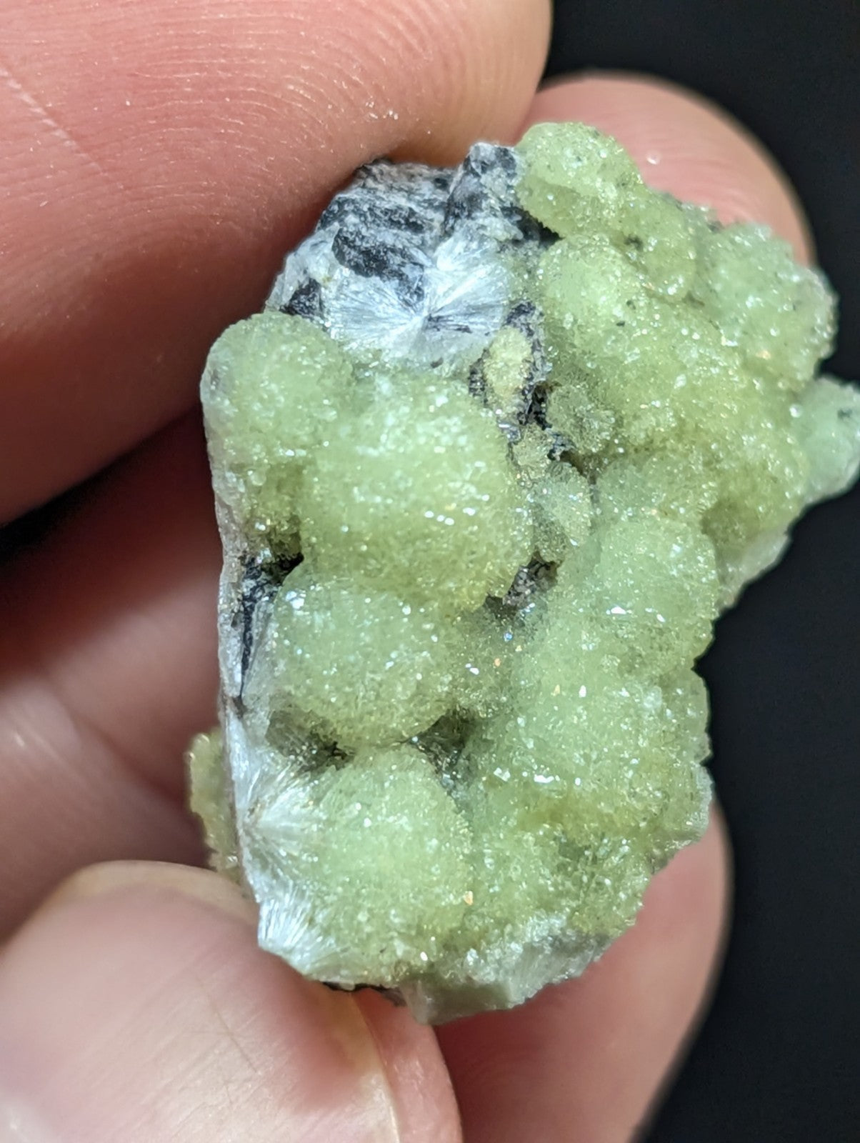 A cluster of translucent, pale green crystals with a rough, textured surface and some white crystalline formations.