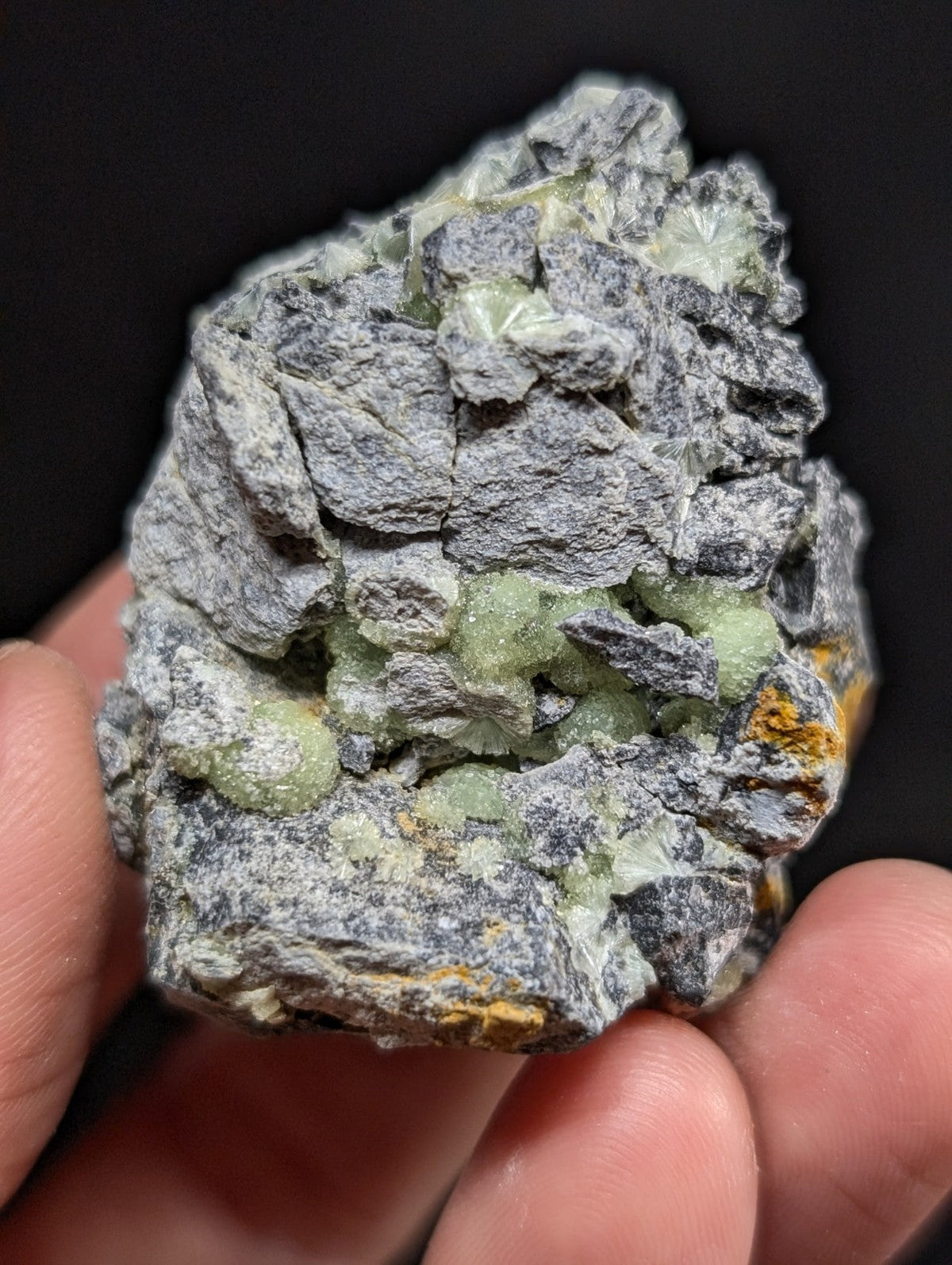 A rough, irregularly shaped mineral specimen featuring a gray matrix with embedded translucent green crystals and small patches of yellowish material.