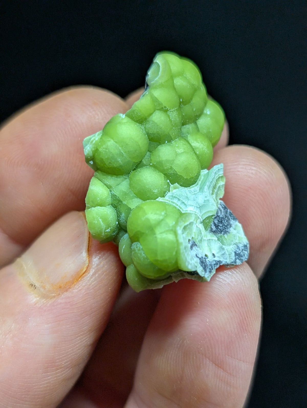 A vibrant green, bumpy mineral specimen with a glossy surface and some white crystalline patterns.