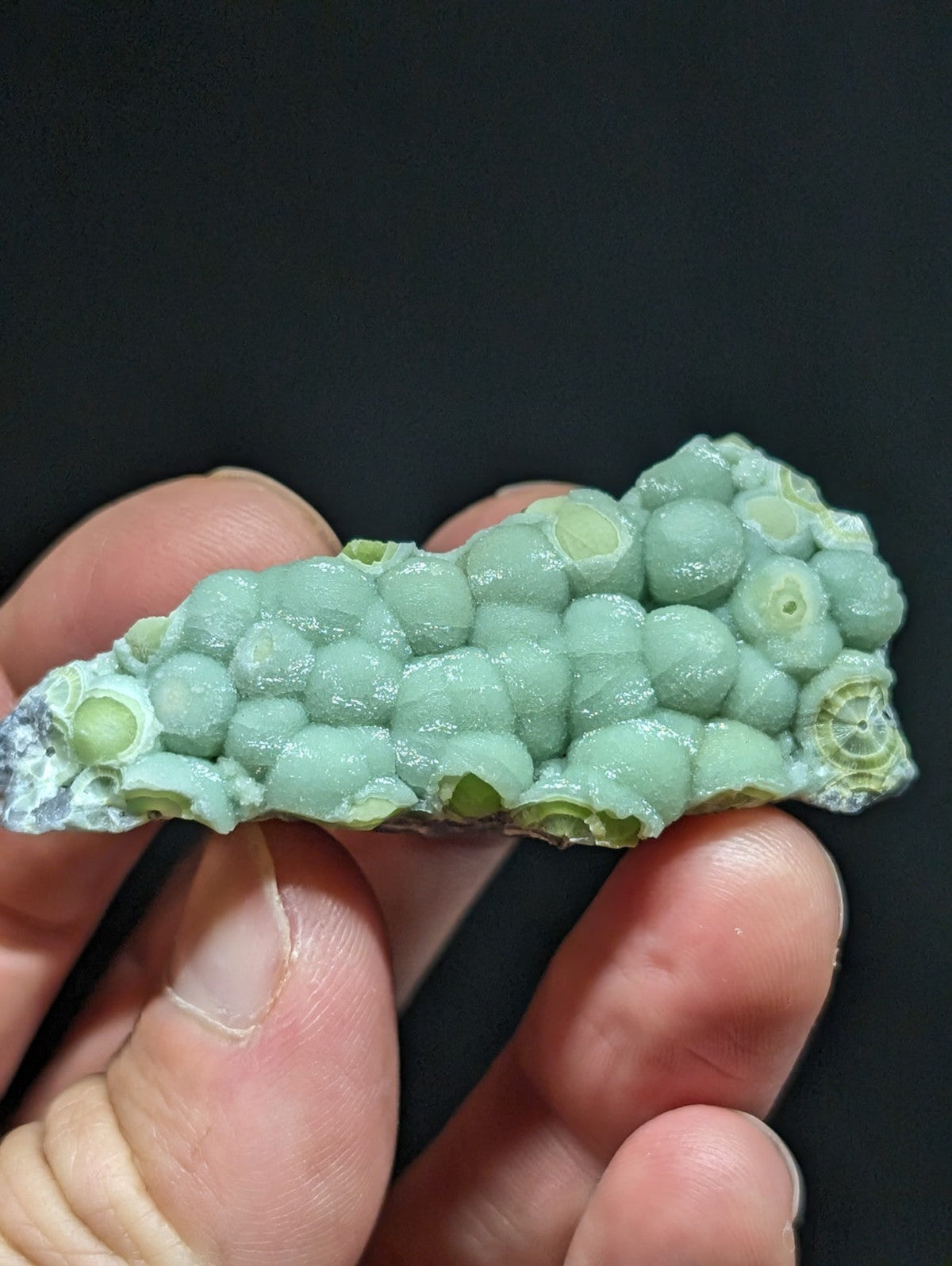 A pale green, translucent mineral specimen featuring a cluster of rounded, bubble-like formations with concentric rings visible within each.