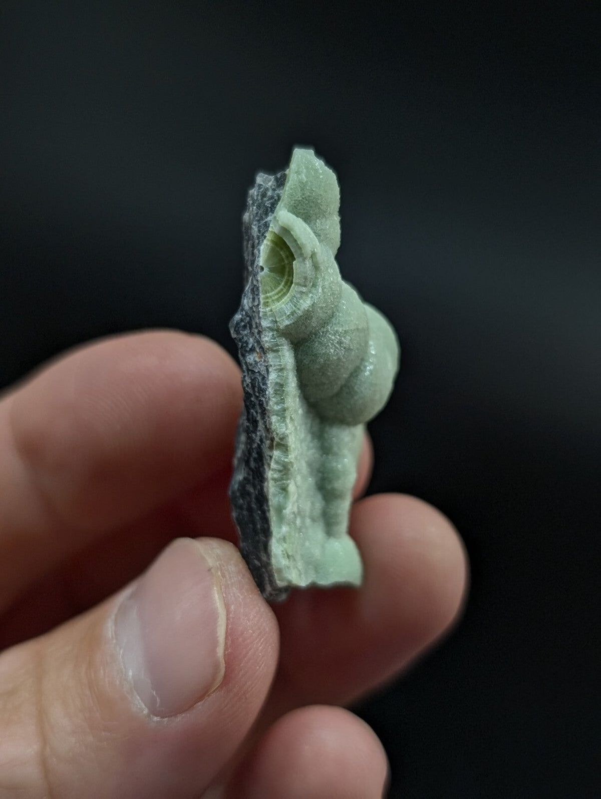 A pale green, translucent mineral specimen with a smooth, rounded form and visible internal concentric layers.