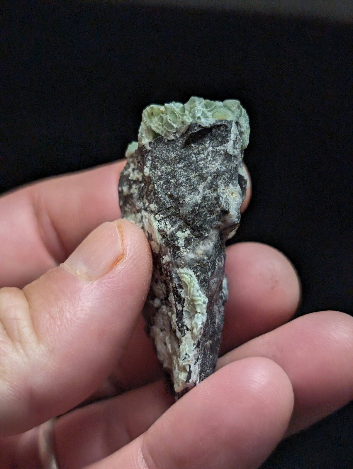 A rough, irregularly shaped mineral specimen with a mottled green and dark gray surface.