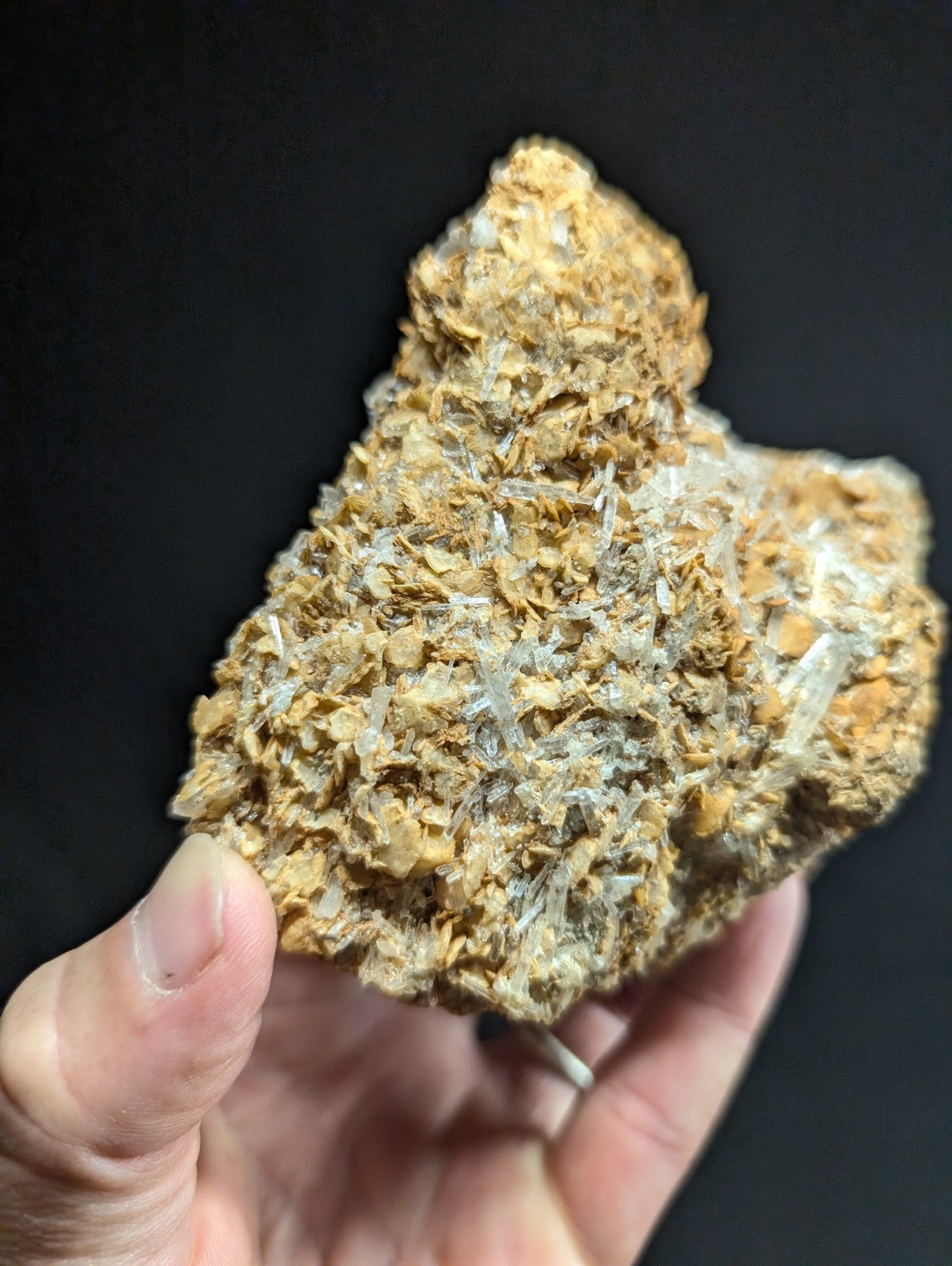 A hand holds a rough, earthy-brown rock specimen featuring translucent quartz crystals embedded within its matrix.