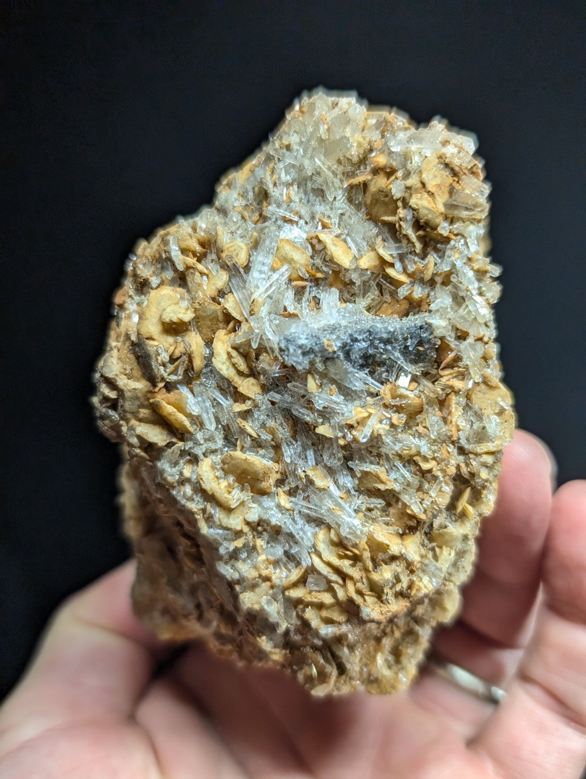 A hand holds a rough, irregularly shaped mineral specimen featuring translucent quartz crystals intergrown with golden-brown matrix material.