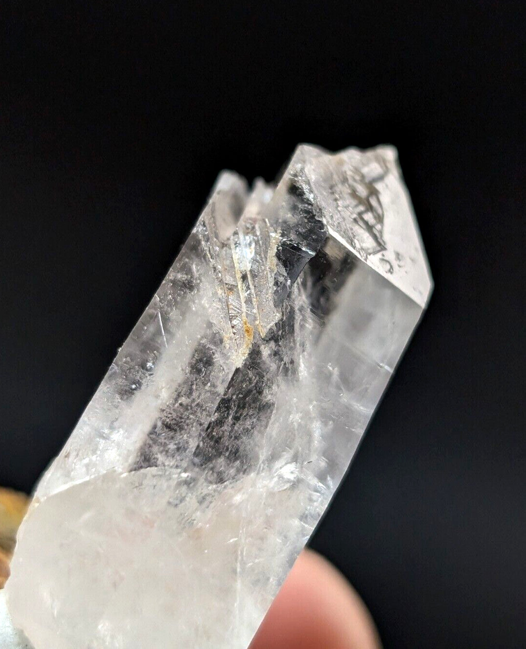 A clear quartz crystal with natural inclusions and a faceted, pointed top.