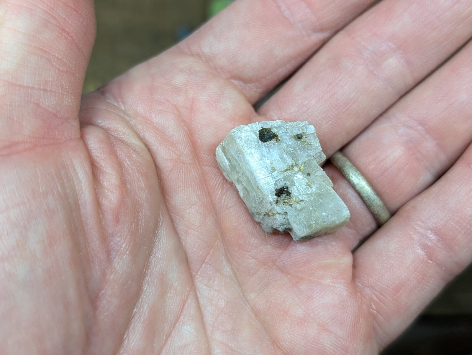 A light gray, rough-textured mineral specimen with dark inclusions resting in an open palm.