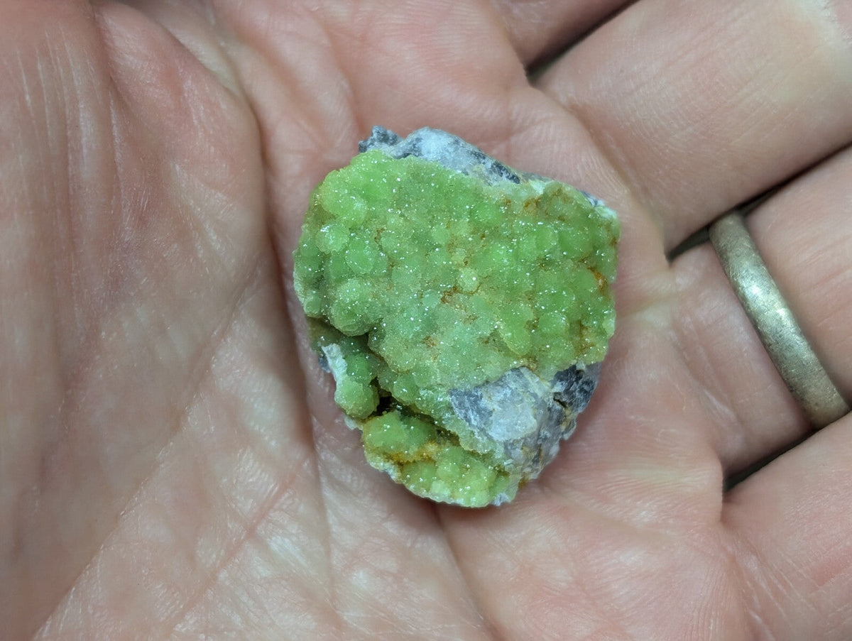 A vibrant green, crystalline mineral specimen with a textured surface and hints of white and yellowish matrix.