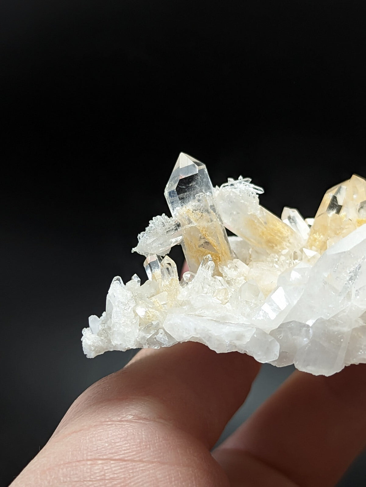 A translucent quartz crystal cluster with clear and golden-yellow facets, held delicately in a hand.