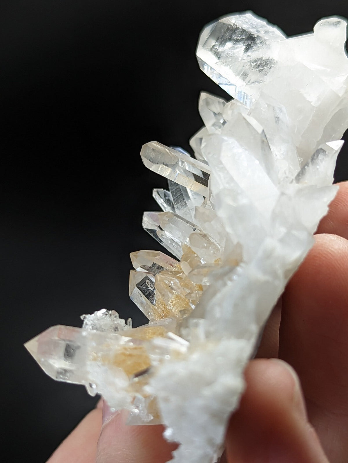 A cluster of clear, translucent quartz crystals with some exhibiting a subtle golden hue and others displaying white crystalline formations.