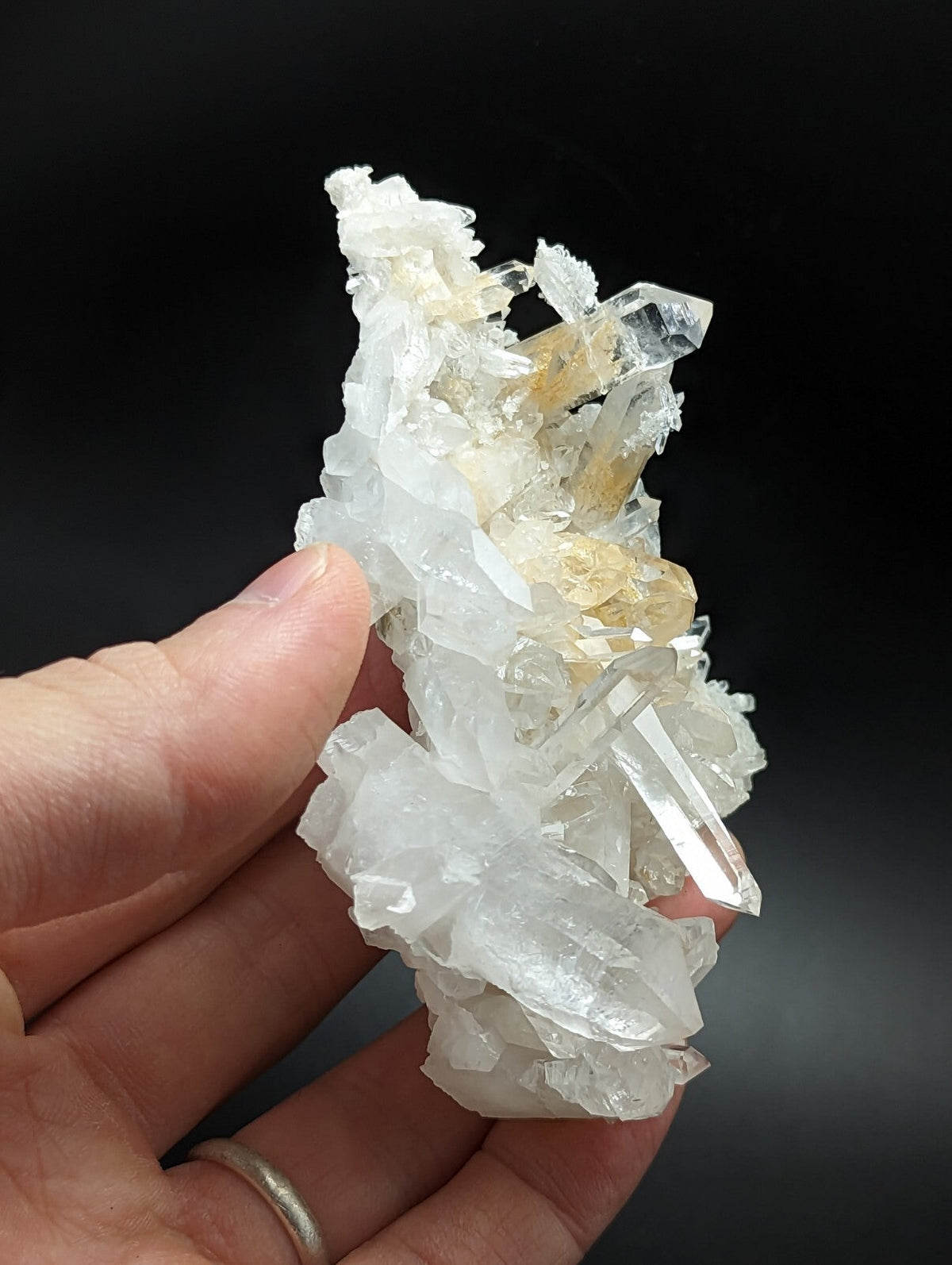 A translucent white and golden crystal cluster with sharp, faceted points held in a hand.