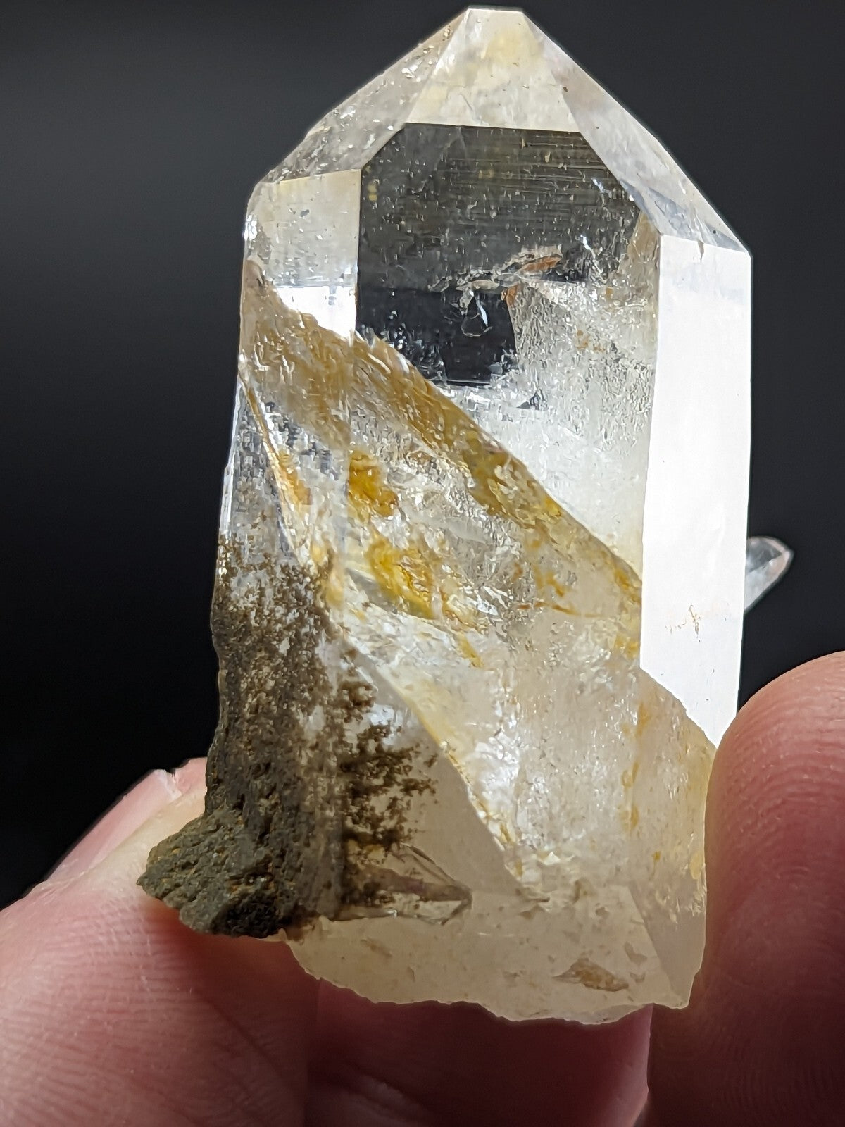 A clear, translucent quartz crystal with golden inclusions and a dark mineral base.