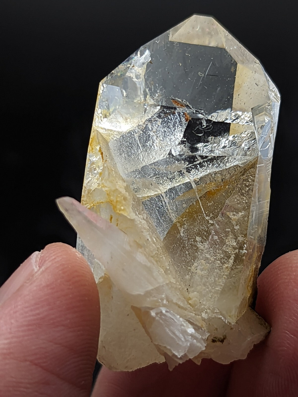 A translucent, pale yellow crystal with a faceted top and rougher base, held between fingers.