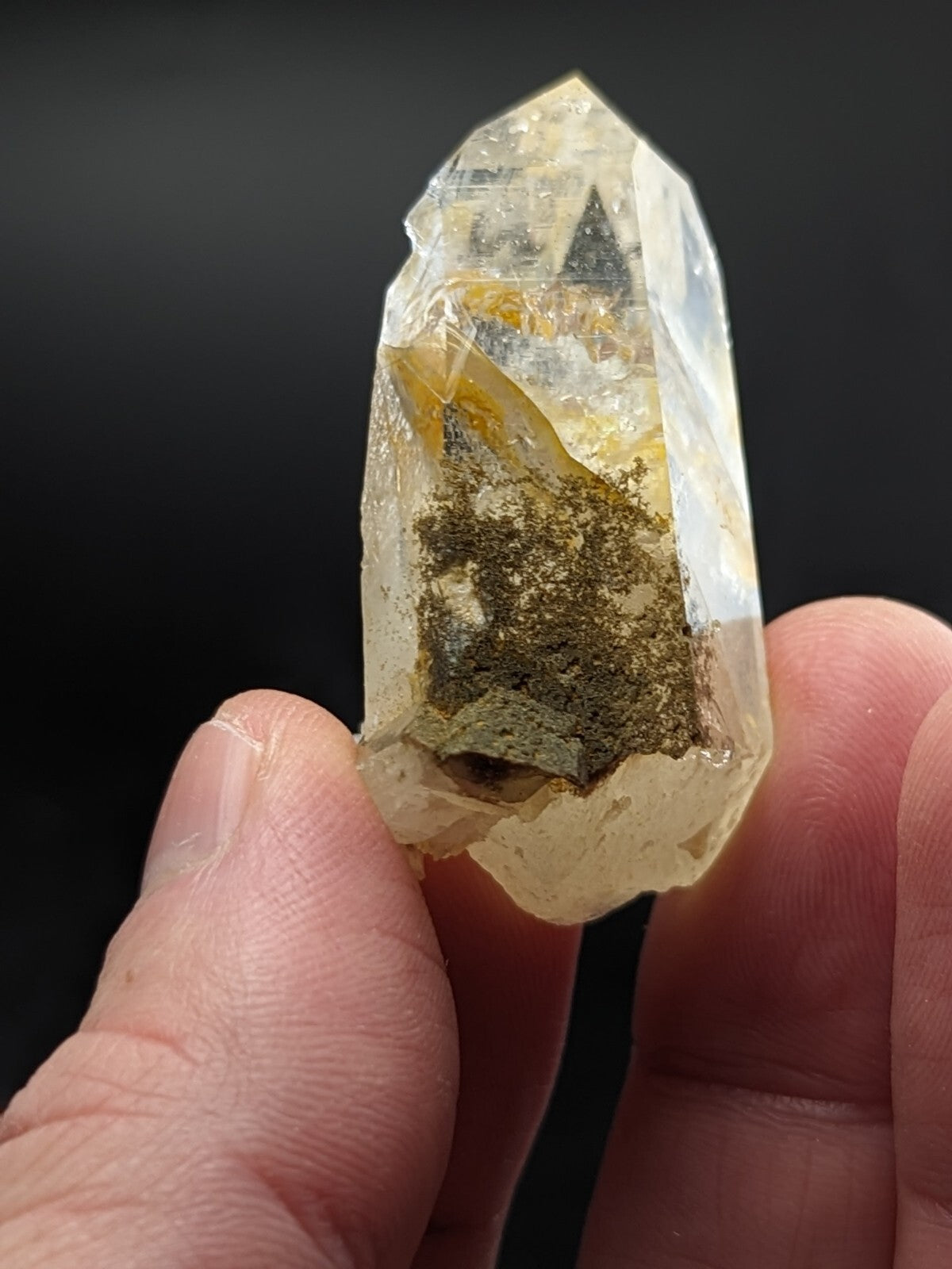 A translucent, pale yellow crystal with a pointed tip and internal greenish-brown inclusions.