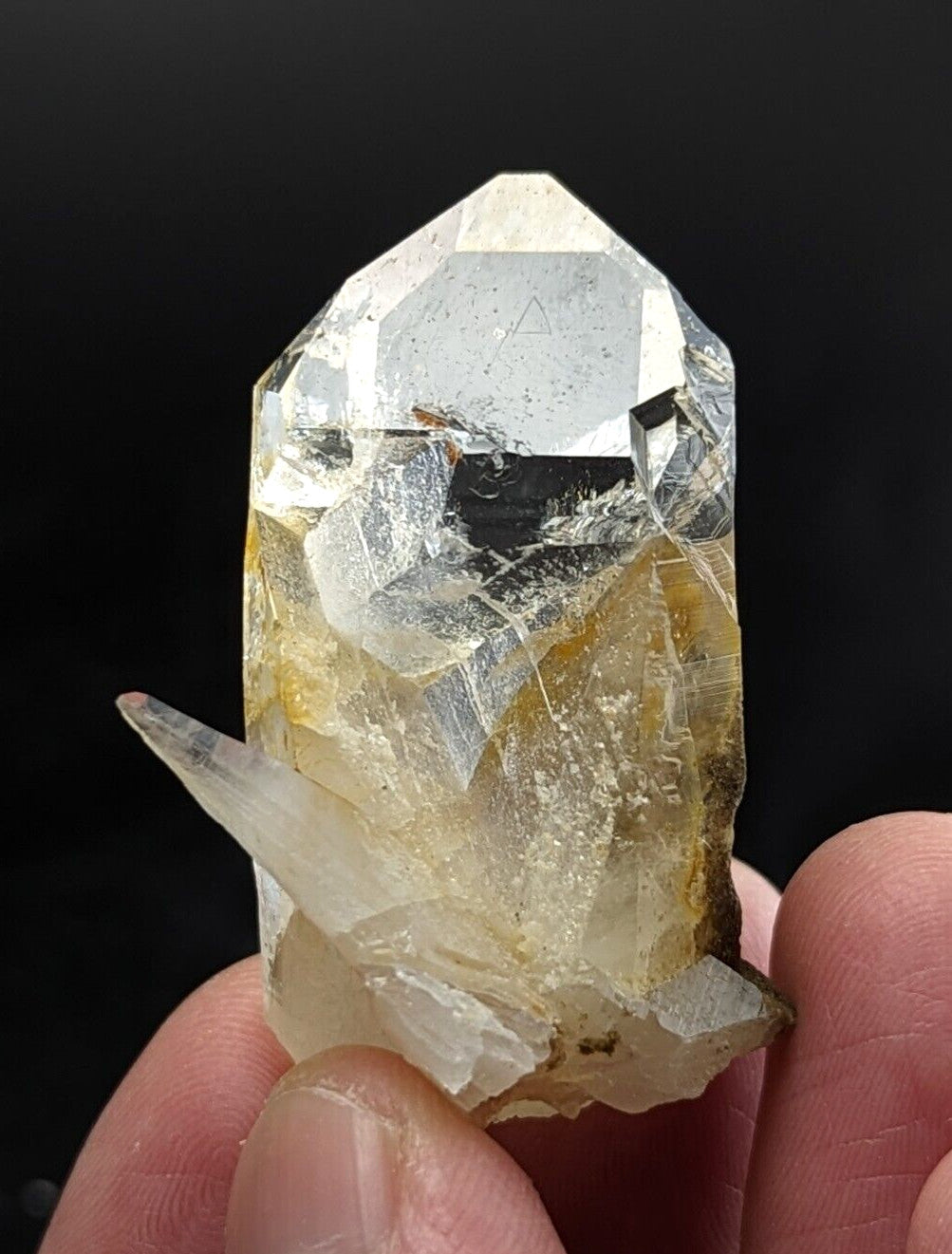 A translucent yellowish quartz crystal with a pointed top and natural inclusions, held gently between fingers.
