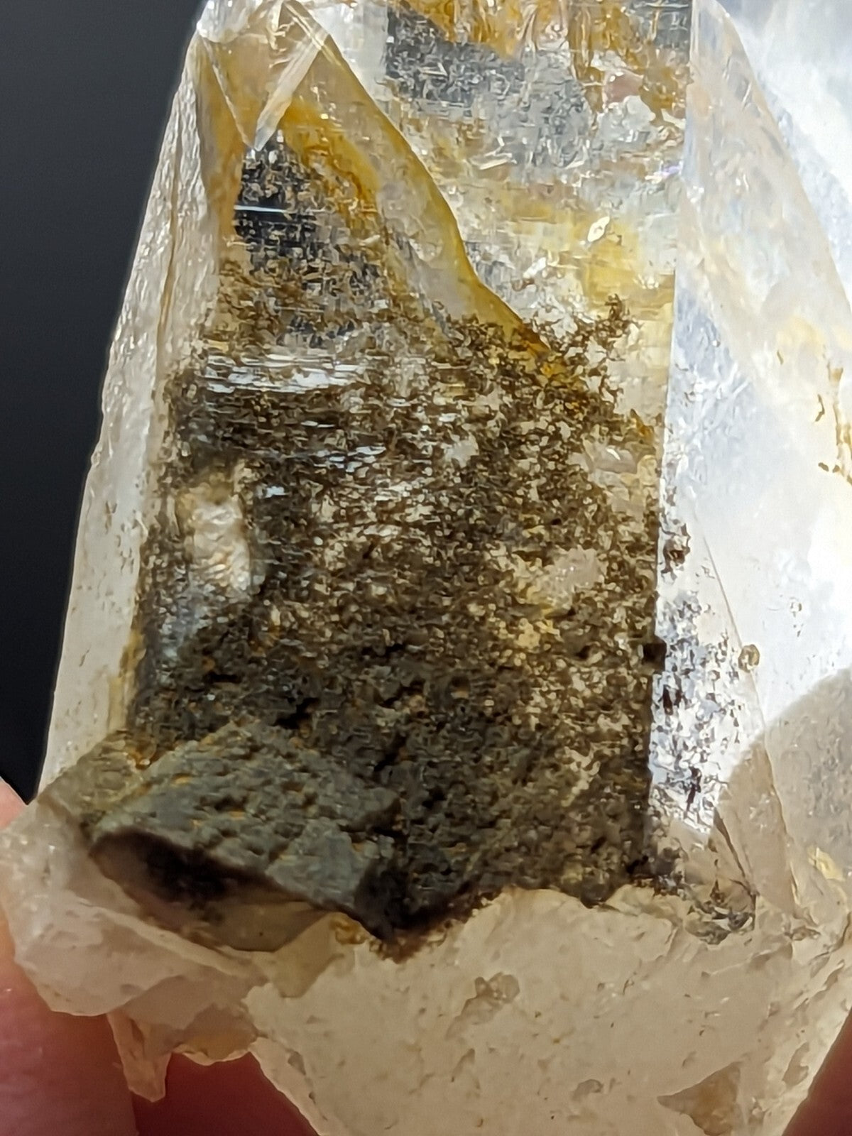 A translucent quartz crystal with a golden-yellow hue, featuring embedded dark green and black mineral inclusions.