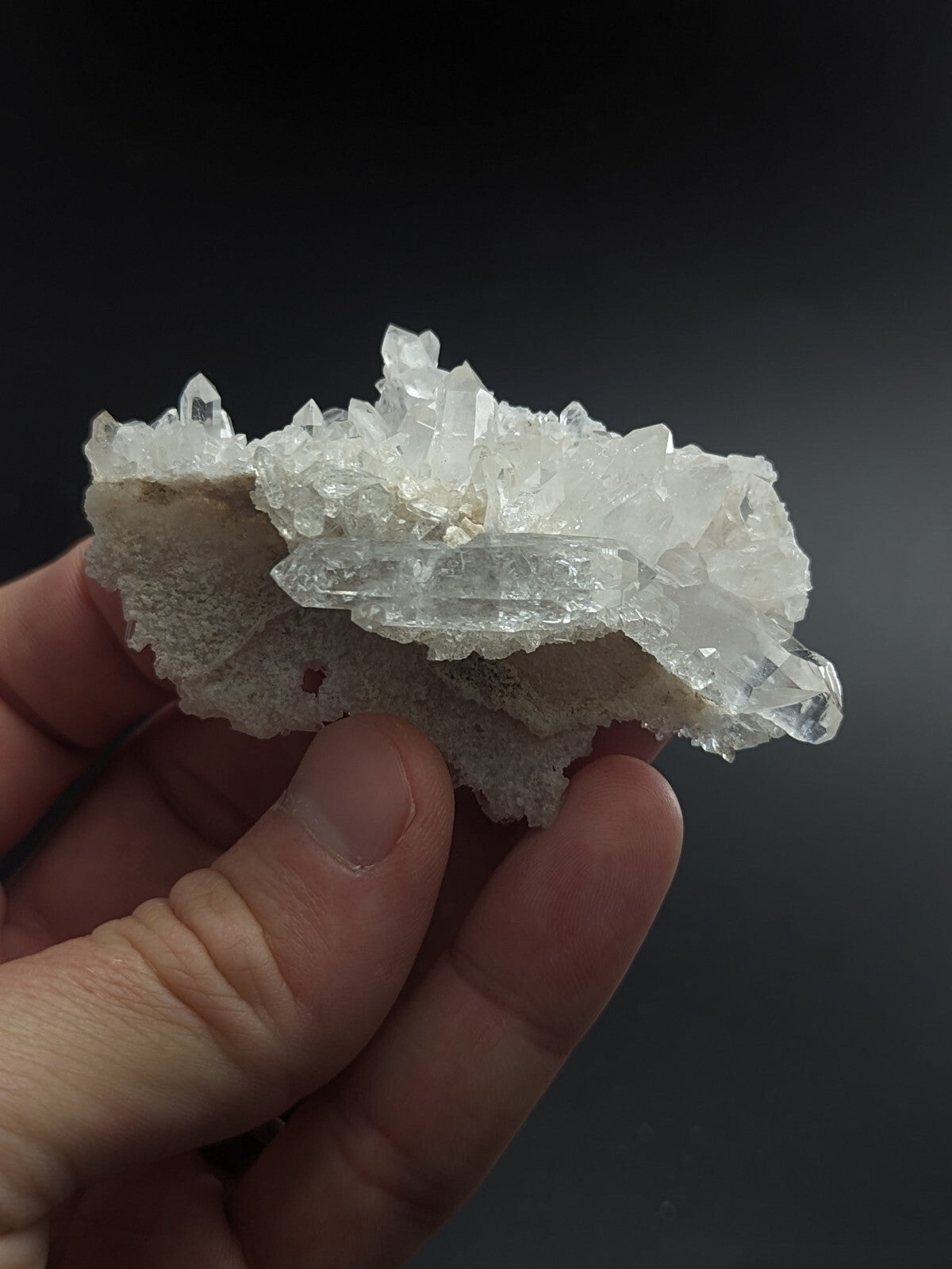 A translucent white quartz crystal cluster with sharp, faceted points emerging from a rougher, lighter-colored matrix.