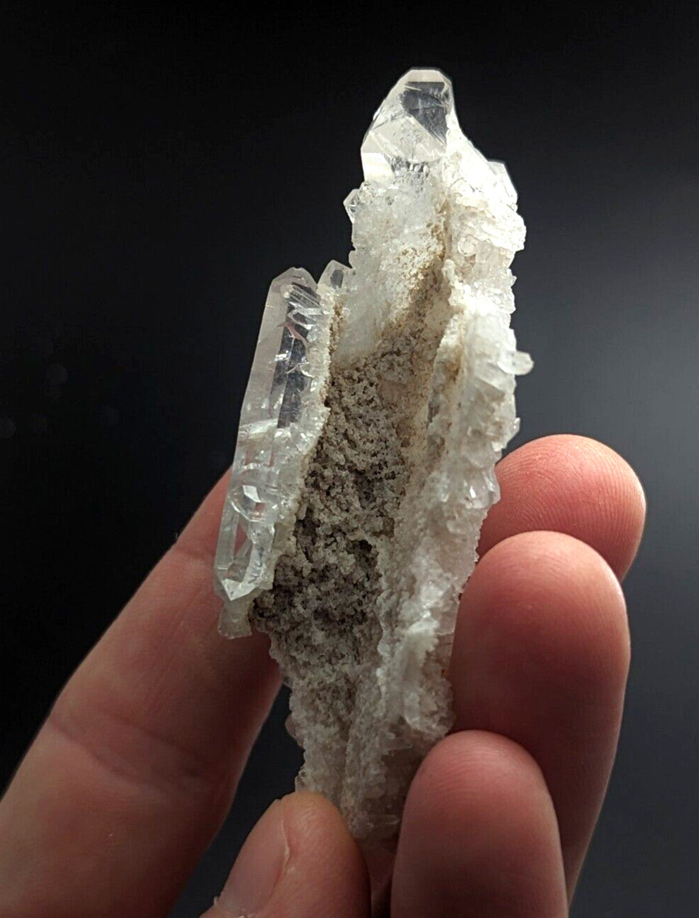 A translucent, crystalline quartz specimen with sharp facets and a central band of grayish matrix material.