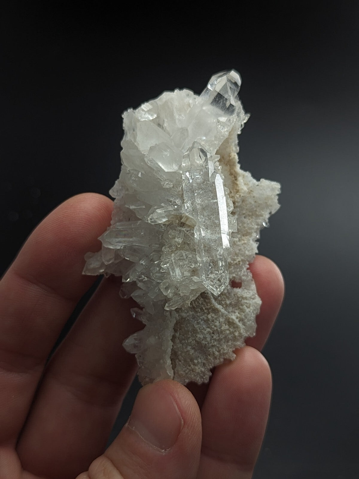 A translucent, clear quartz crystal cluster with sharp facets and a rough, white matrix base.