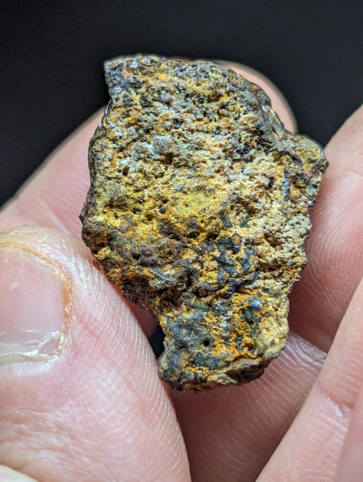 A rugged, irregularly shaped meteorite fragment with a textured surface displaying patches of yellowish-orange and dark brown rust-like patina.