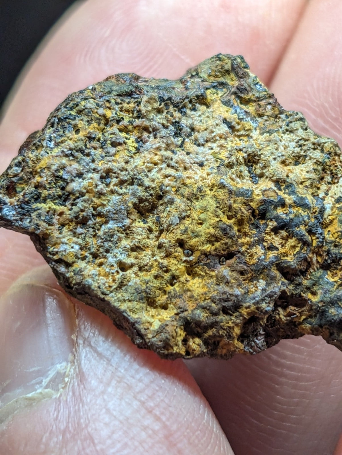 A rugged, irregularly shaped meteorite fragment with a textured surface displaying patches of yellowish-green patina and dark gray to black areas.