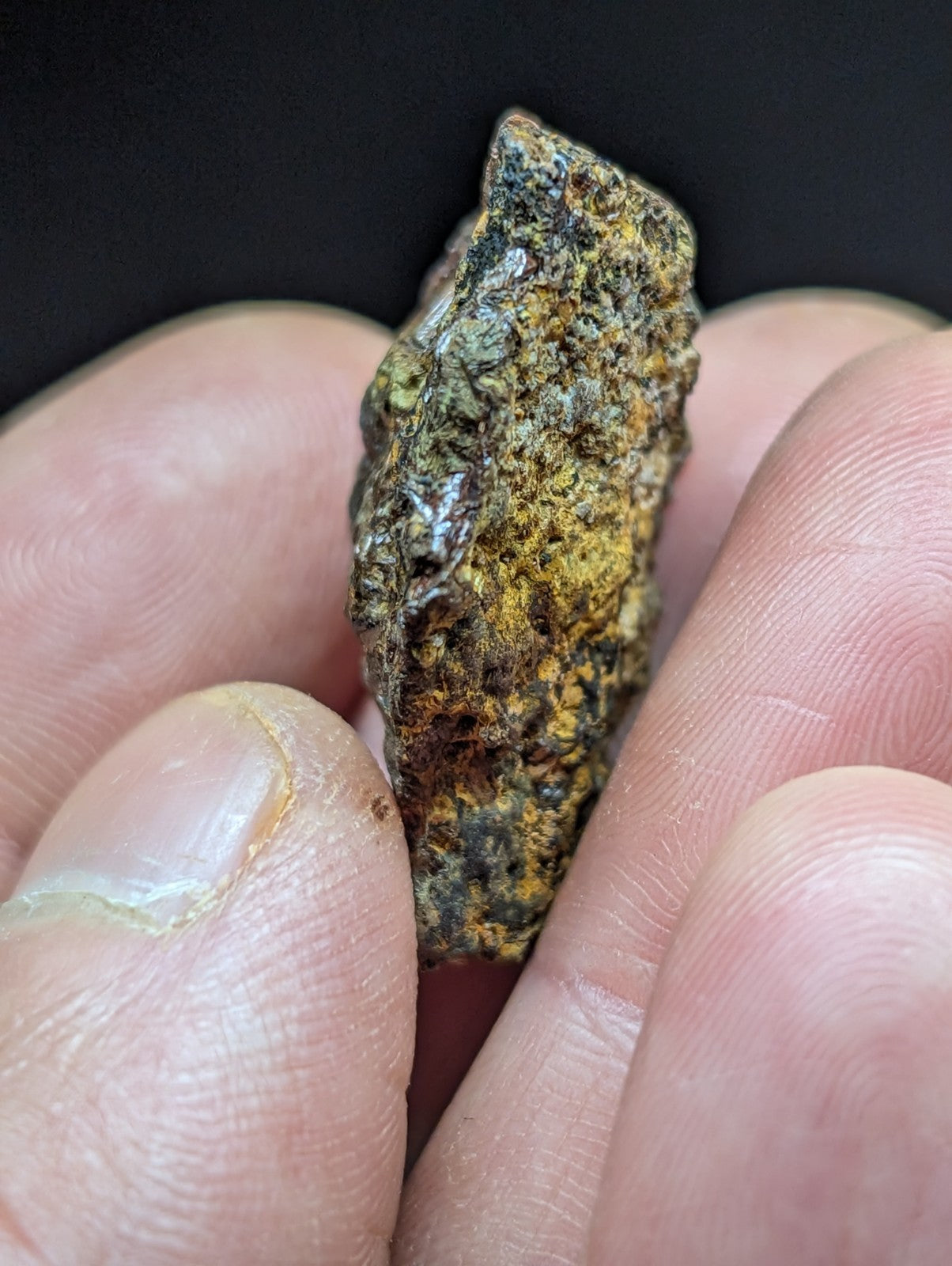 A rugged, irregularly shaped meteorite with a mottled surface of dark brown and vibrant yellow-green patina.