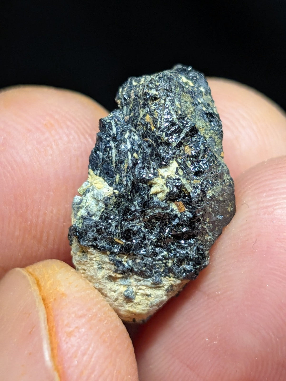 A rough, irregularly shaped mineral specimen with a dark black and greenish-gray surface, featuring patches of lighter yellowish material.