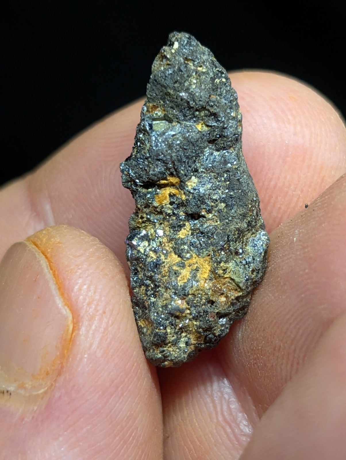 A rugged, dark gray metallic mineral specimen with patches of vibrant yellow and subtle greenish hues.