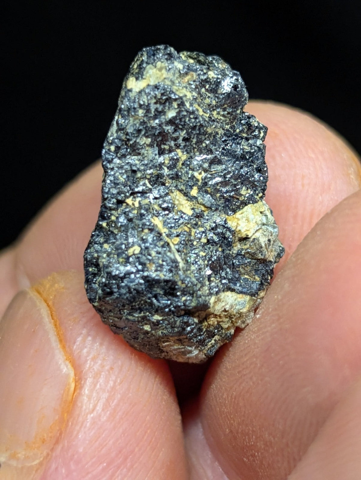 A rough, irregularly shaped mineral specimen with a dark gray surface speckled with patches of yellowish-gold.