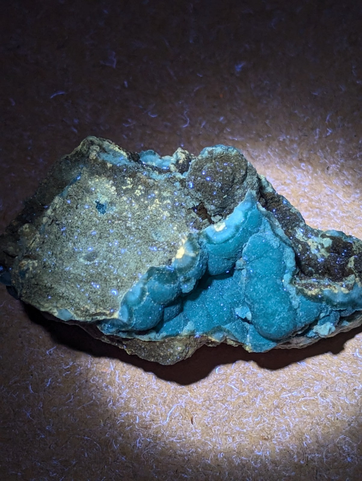 A vibrant turquoise mineral specimen with a rough, irregular surface and patches of dark matrix.