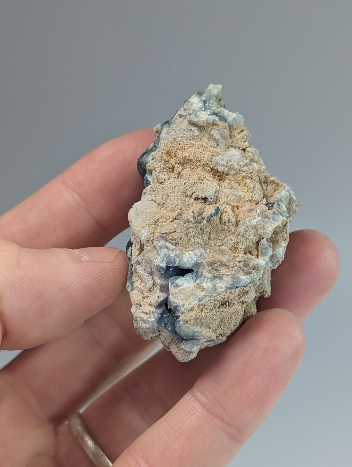 A rough, irregularly shaped mineral specimen with patches of blue and gray hues embedded in a tan matrix.