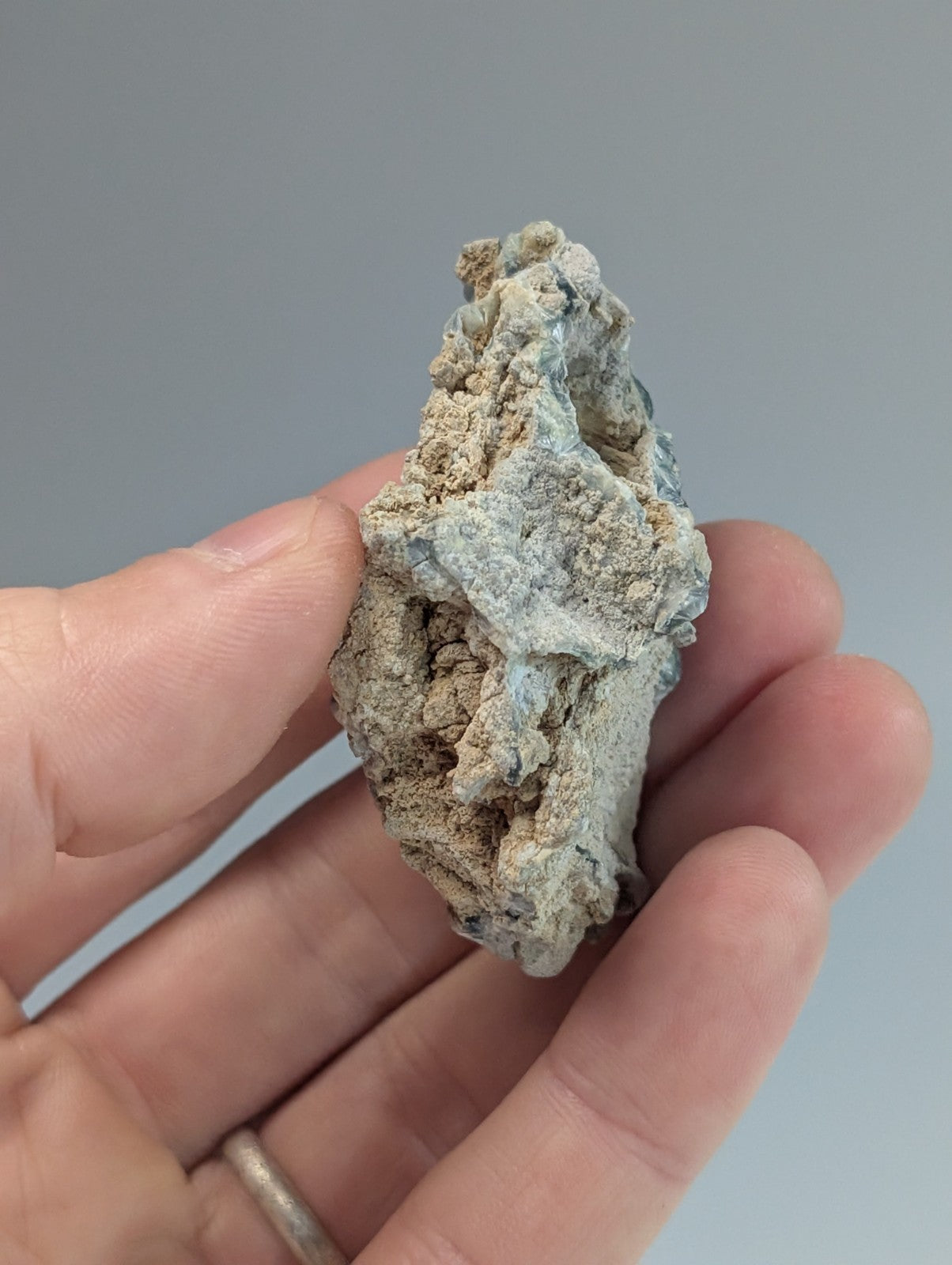 A textured, irregularly shaped mineral specimen with a mottled gray and light blue surface.