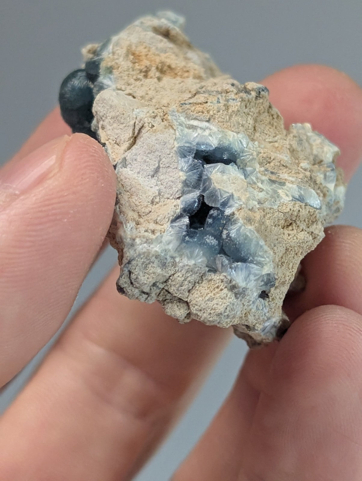 A hand holds a rough, light gray rock with intricate blue and white crystalline formations inside.